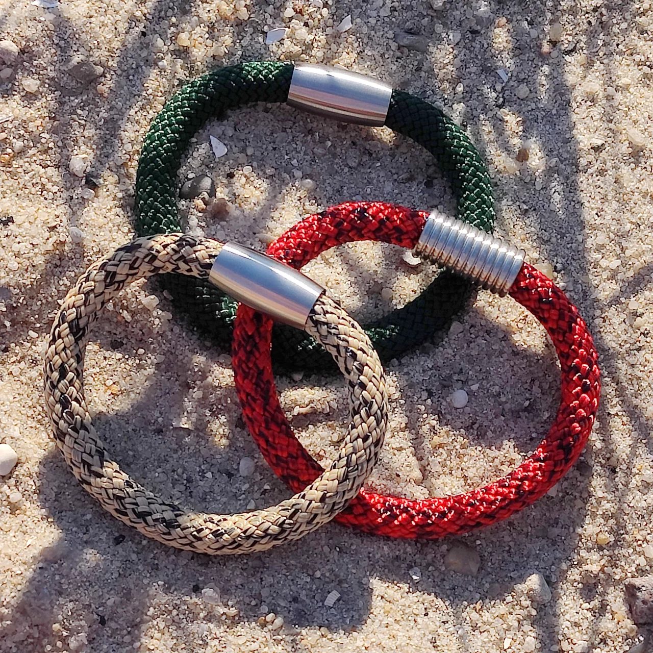 Klabautermann-Armbänder aus Paracord in Grün, Rot und Natur mit Edelstahl-Magnetverschluss auf Sand